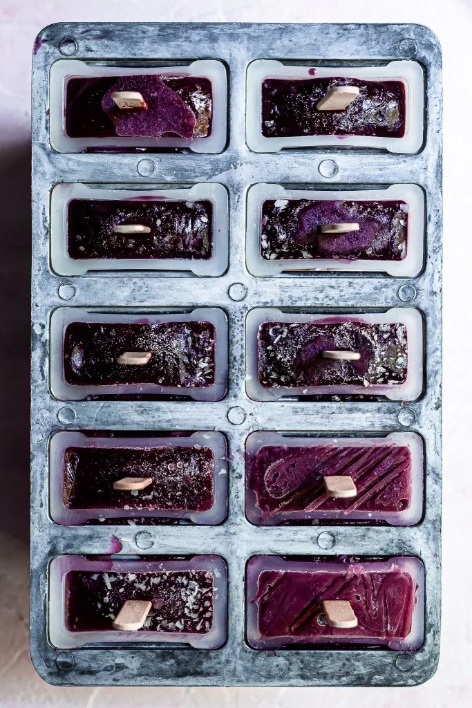 View looking down on popsicle mold straight out of the freezer containing purple popsicles with flecks of ice and frost on the surface