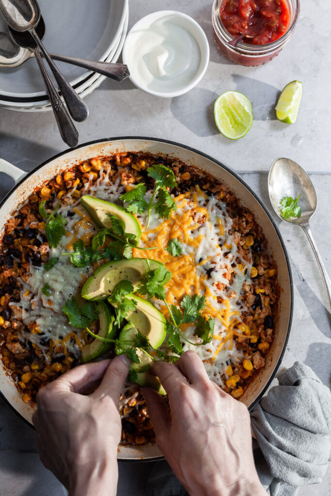 Hands garnishing a rice skillet with avocado and cilantro