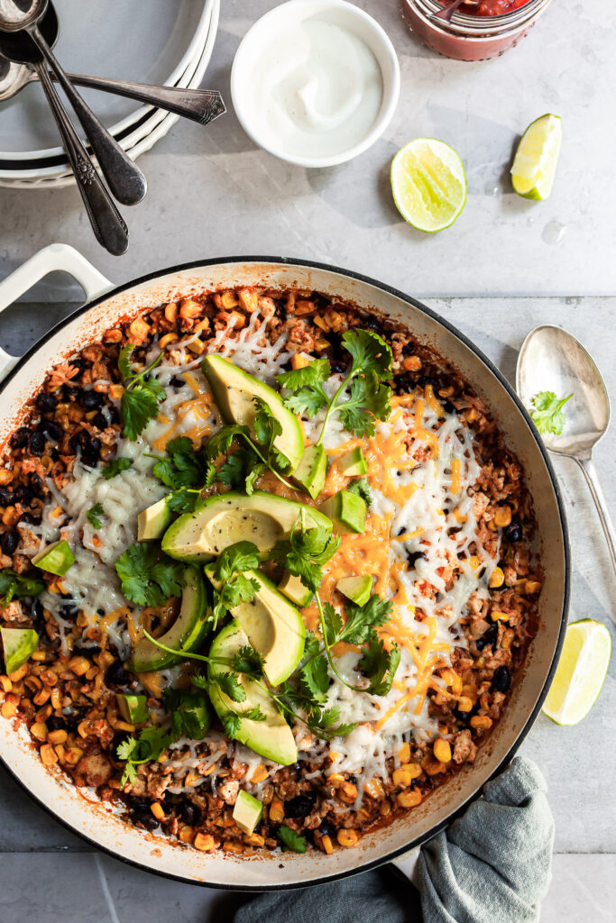 White enamel skillet filled with rice, beans and corn, garnished with avocado and cilantro