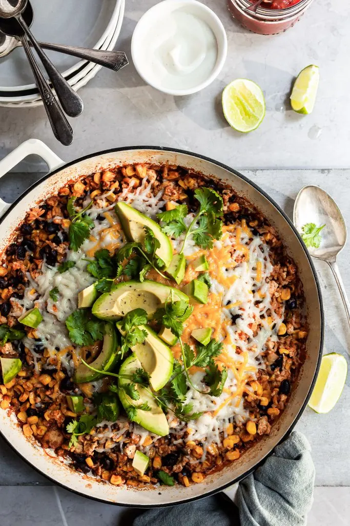White enamel skillet filled with rice, beans and corn, garnished with avocado and cilantro