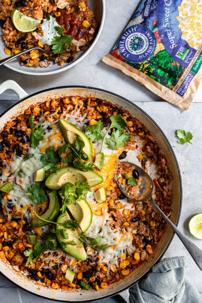 Baked rice with black beans and corn in a white skillet with a white bowl containing a serving