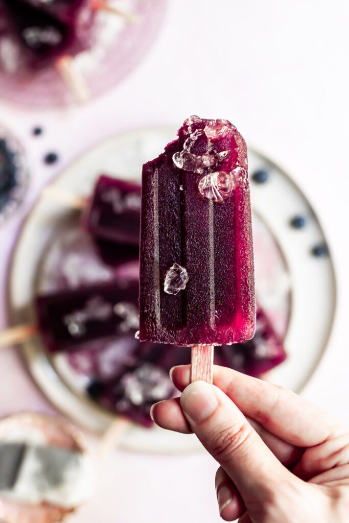 a bite taken from purple popsicle garnished with a few small pieces of ice 