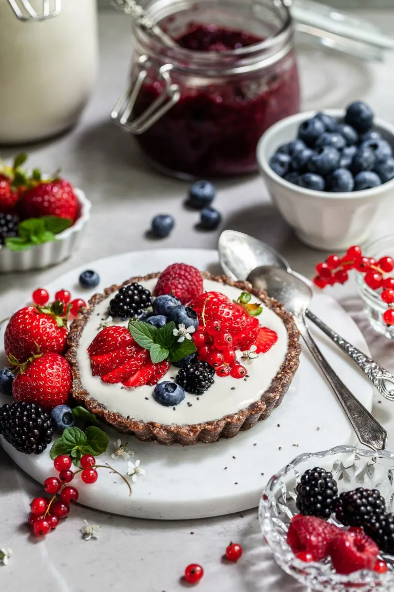 Breakfast table scene with a small tart willed with yogurt and topped with fresh berries