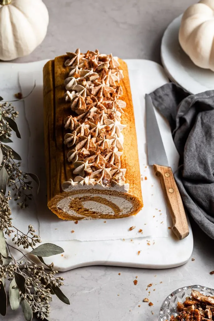 Unsliced pumpkin cake roll on a white marble platter 