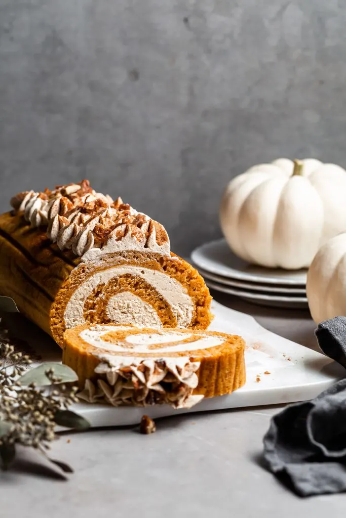 pumpkin swiss roll on a white platter with a single slice cut