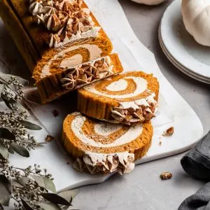 pumpkin roll on a white plater beside 2 small white pumpkins