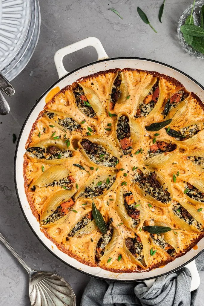 Baked pasta shells in a large white skillet garnished with fried sage
