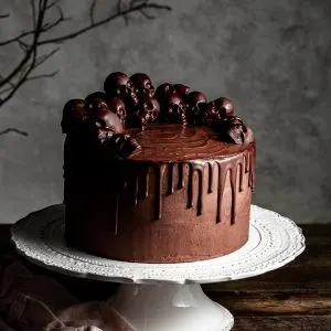 Chocolate layer drip cake decorated with small chocolate skulls, sitting on a white cake stand