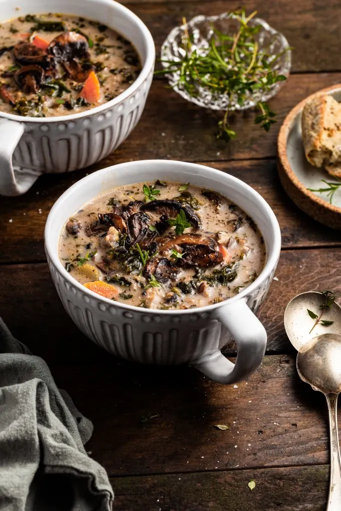 Large cup of mushroom soup beside a plate of crusty bread