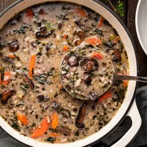 A white enamel cast iron pot filled with mushroom rice soup, being ladled out.
