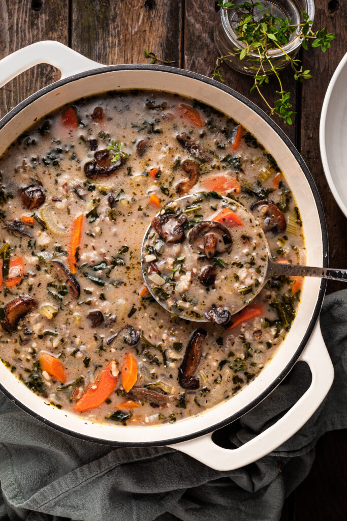 A white enamel cast iron pot filled with mushroom rice soup, being ladled out.
