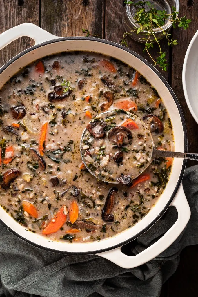 A white enamel cast iron pot filled with mushroom rice soup, being ladled out.