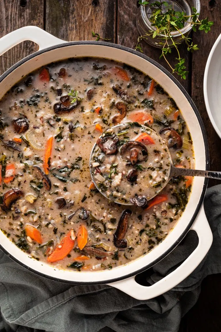 A white enamel cast iron pot filled with mushroom rice soup, being ladled out.