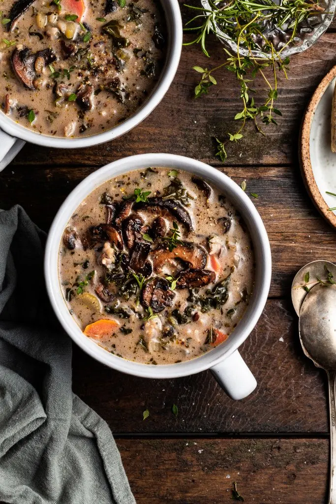 Flatlay of two large mugs filled with vegan mushroom rice soup, topped with fried mushrooms and fresh herbs
