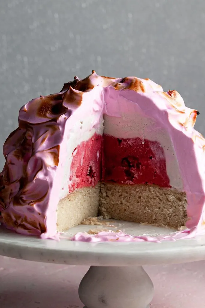 Close up of the inside of a baked Alaska revealing layers of vanilla and raspberry sorbet over vanilla cake