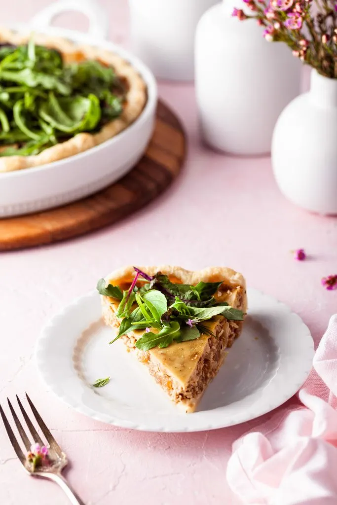 Slice of vegan French onion tart on a white plate topped with fresh herbs. 