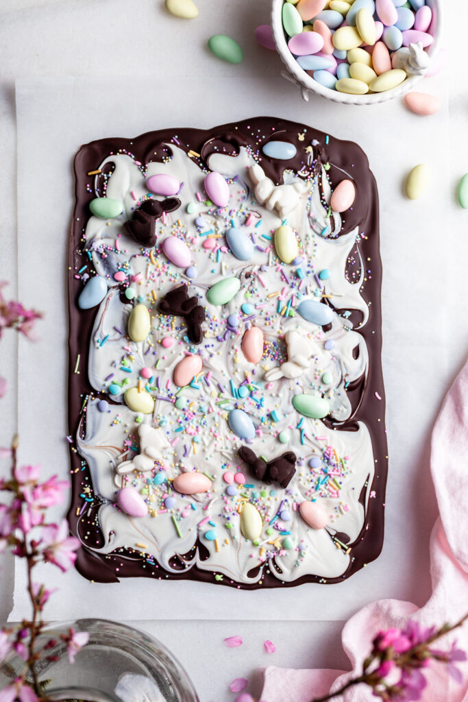 Chocolate bark made with dark chocolate layered with white chocolate and topped with pastel candy coated almonds on a white marble slab