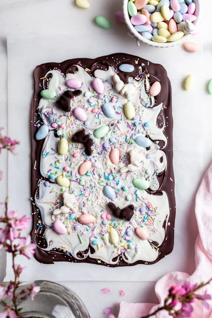 Chocolate bark made with dark chocolate layered with white chocolate and topped with pastel candy coated almonds on a white marble slab