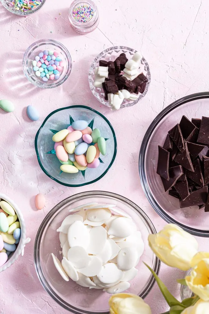 The ingredients for chocolate bark are laid out in bowls on a pink counter. 