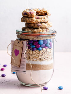 A jar filled with cookie mix, topped with baked vegan m&m cookies.