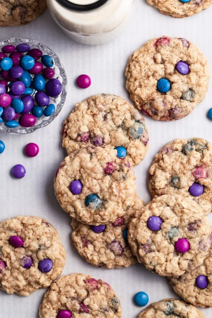 A parchment lined baking tray covered in polka dot cookies, a small bowl of candies and a bottle of milk.