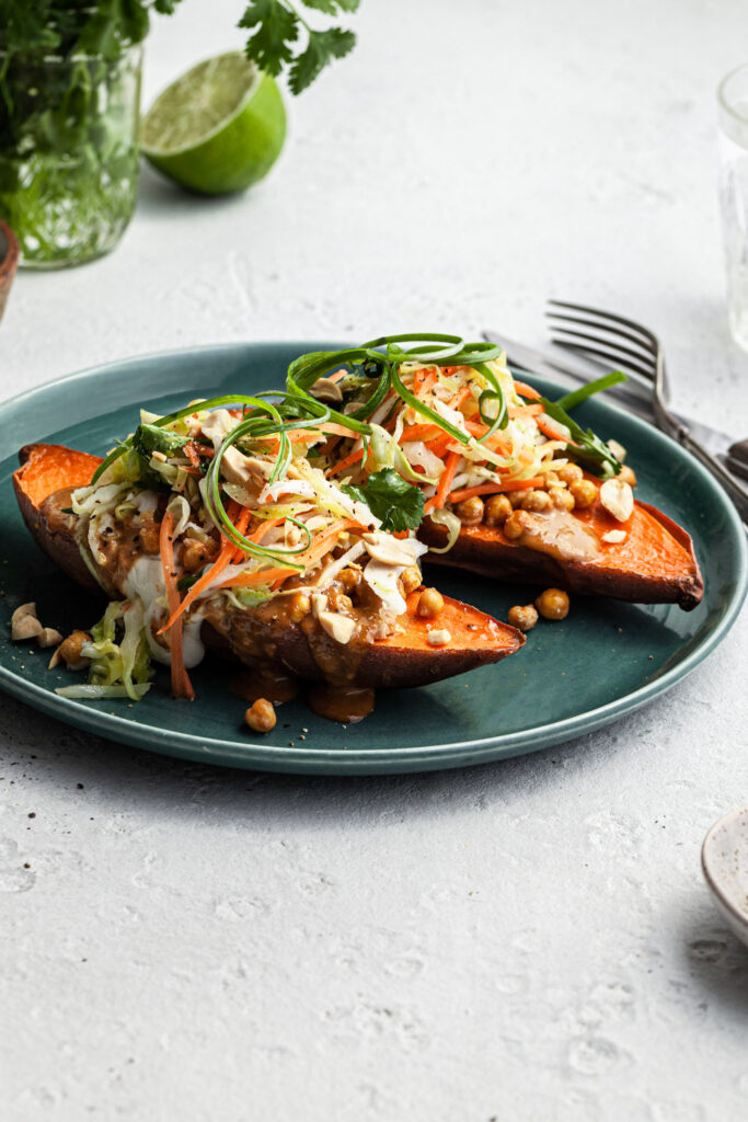 Side view of a green plated filled with two halves of a baked sweet potato stuffed with crispy chickpeas, Thai curry peanut sauce and a simple cabbage slaw. 