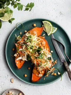 View looking down on a green plate filled with a sweet potato cut in half, topped with cripsy chickpeas, peanut sauce and coleslaw.