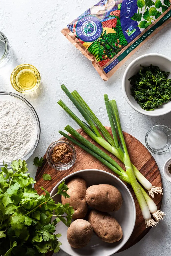 An image showing the ingredients for the stuffed flatbread including potatoes, spinach, oil, flour, salt, water, cilantro, spices and green onions.