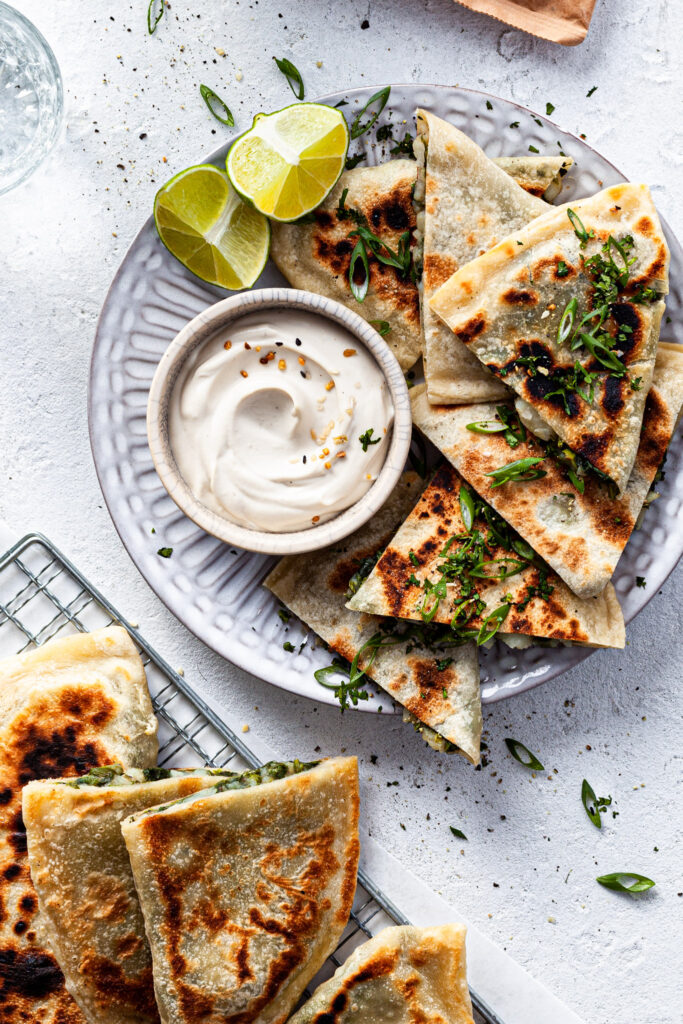A plate filled with stuffed flatbread and a small bowl of white dip.