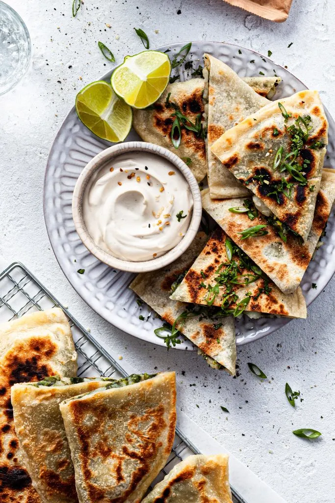A plate filled with stuffed flatbread and a small bowl of white dip.