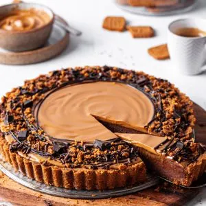 A Vegan chocolate biscoff tart with one slice cut and partly removed to reveal the inside of the tart showing off the chocolate layer topped with cookie butter.