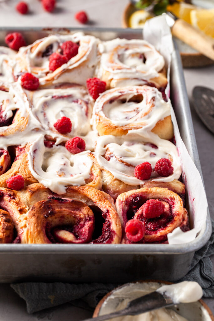 View peeking over the side of the baking tray containing the raspberry sweet rolls, about half of them have been glazed.