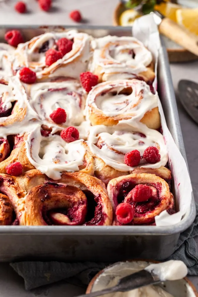 View peeking over the side of the baking tray containing the raspberry sweet rolls, about half of them have been glazed.
