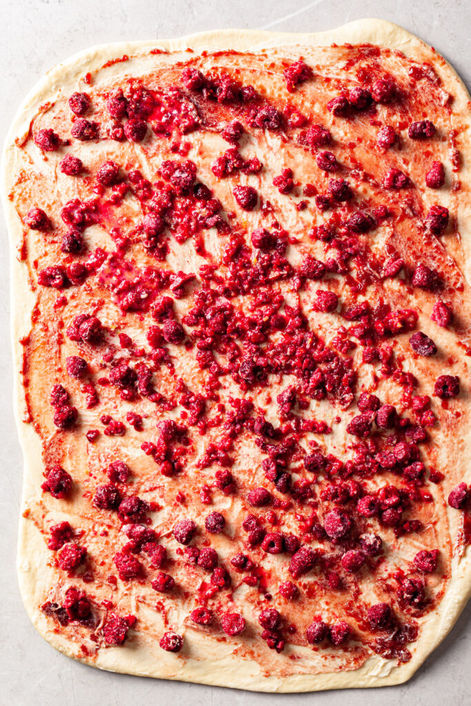 Sweet dough rolled out with vegan butter, raspberry preserves and frozen raspberries spread out on the top. 