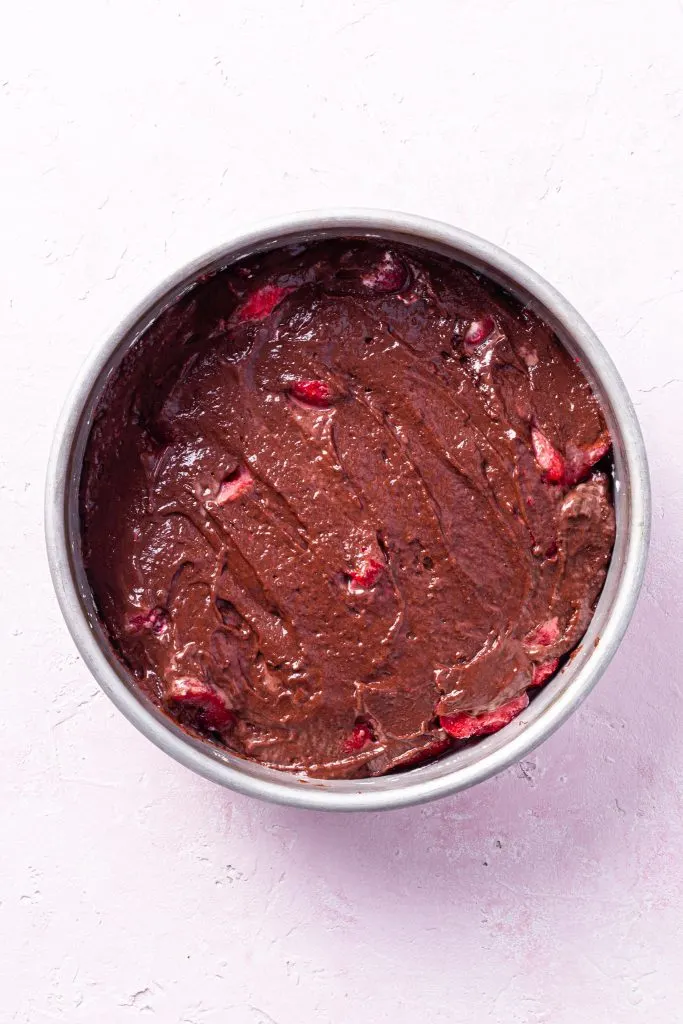 Step 2: A baking dish containing chocolate cake batter spread over strawberries. 