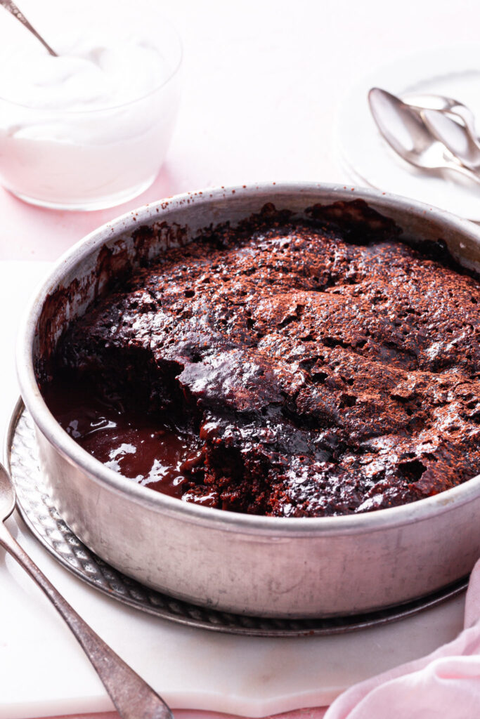 A side view of the self-saucing chocolate strawberry pudding cake with a scoop missing exposing the glossy chocolate sauce on the bottom. 