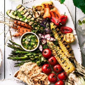 A white platter filled with grilled vegetables covered in avocado chimichurri sauce.