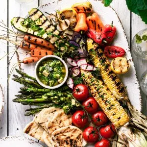A white platter filled with grilled vegetables covered in avocado chimichurri sauce.