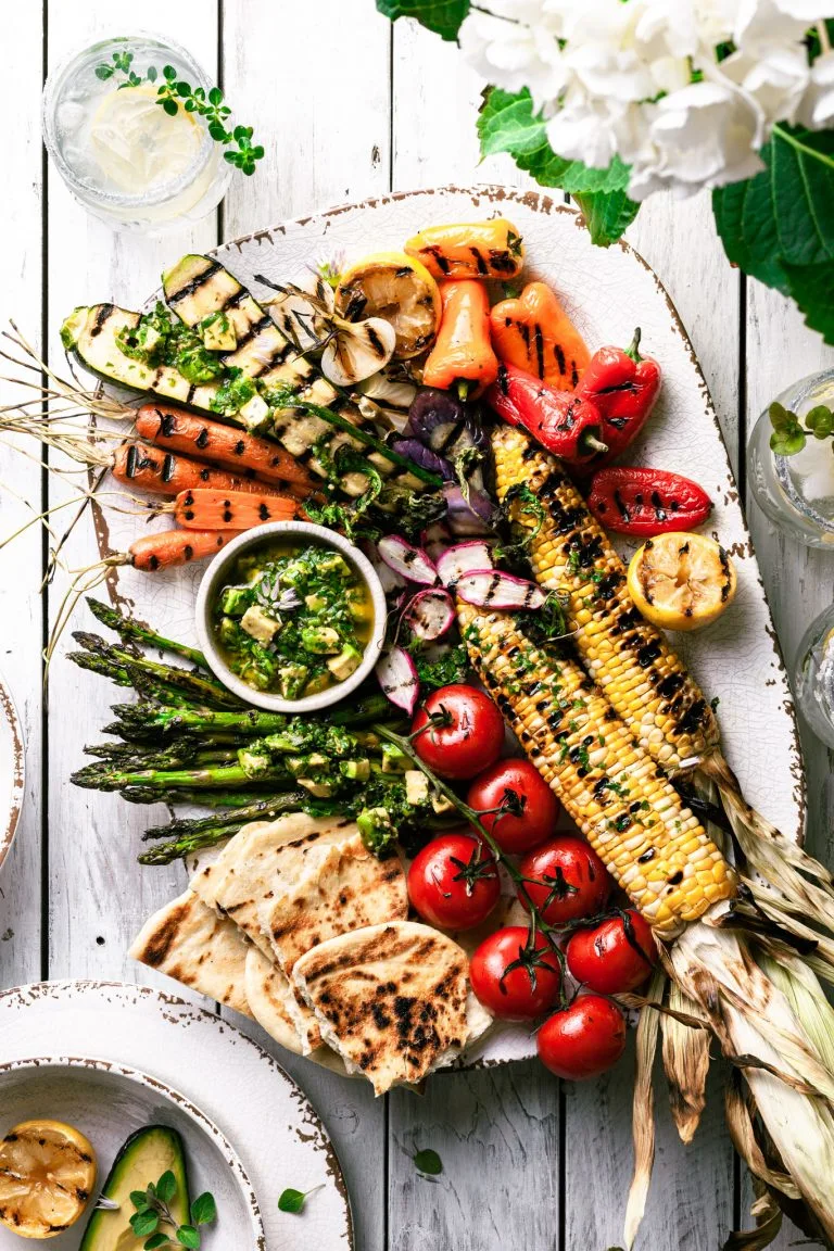 A white platter filled with grilled vegetables covered in avocado chimichurri sauce.