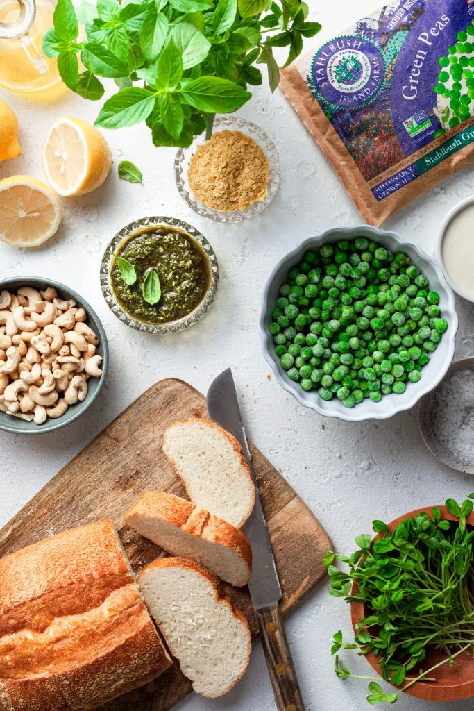 A white counter covered in the ingredients needed for this pesto pea and vegan ricotta toast.