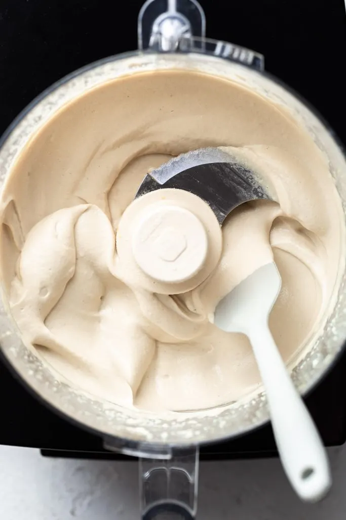 A food processor filled with off-white cashew ricotta which appears to be satiny in texture. 
