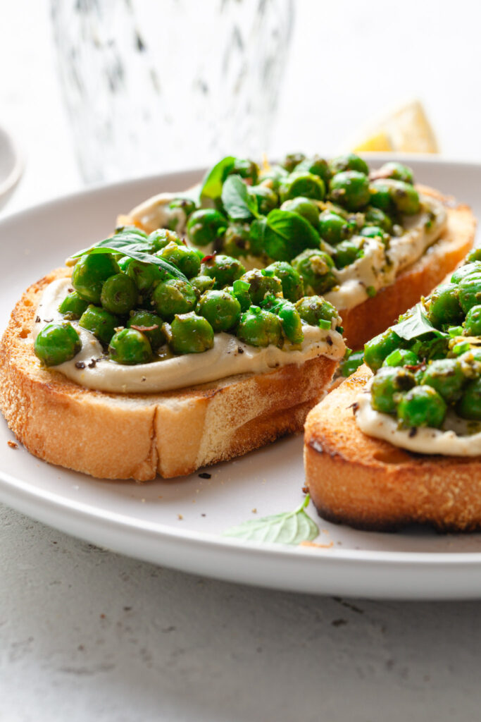 Side view of a piece of toast covered in whipped cashew ricotta, topped with basil peas. 