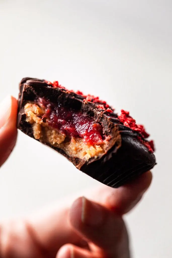 A hand holding a peanut butter and jelly chocolate cup with a bite missing. 