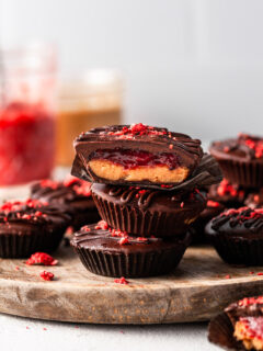 A stack of 3 peanut butter cups featuring a layer of presevres inside, and jars of peanut butter and jam in the background.