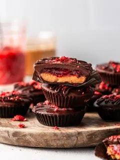 A stack of 3 peanut butter cups featuring a layer of presevres inside, and jars of peanut butter and jam in the background.