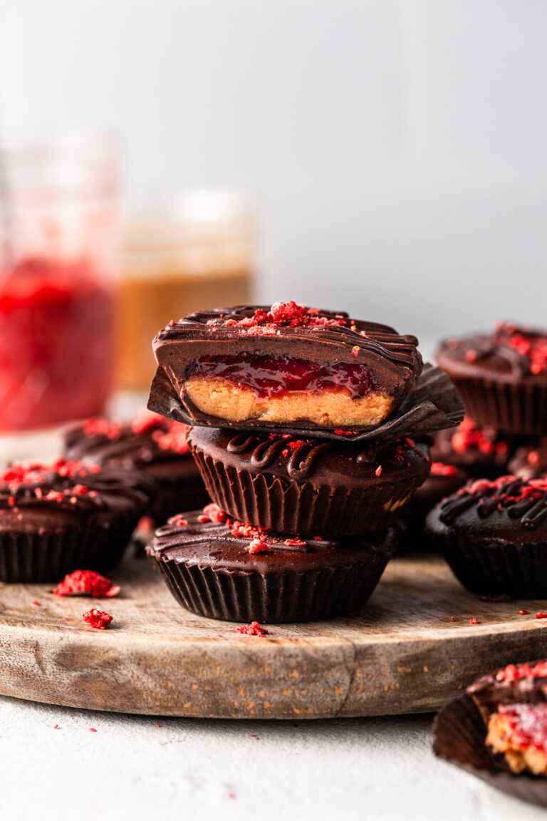 A stack of 3 peanut butter cups featuring a layer of presevres inside, and jars of peanut butter and jam in the background.