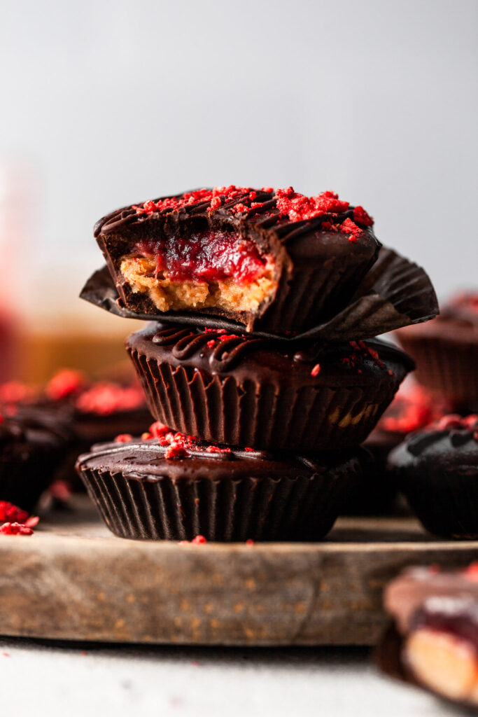 A stack of peanut butter jelly cups on a wooden plate, the top cup has a bite taken out of it revealing the layered filling. 