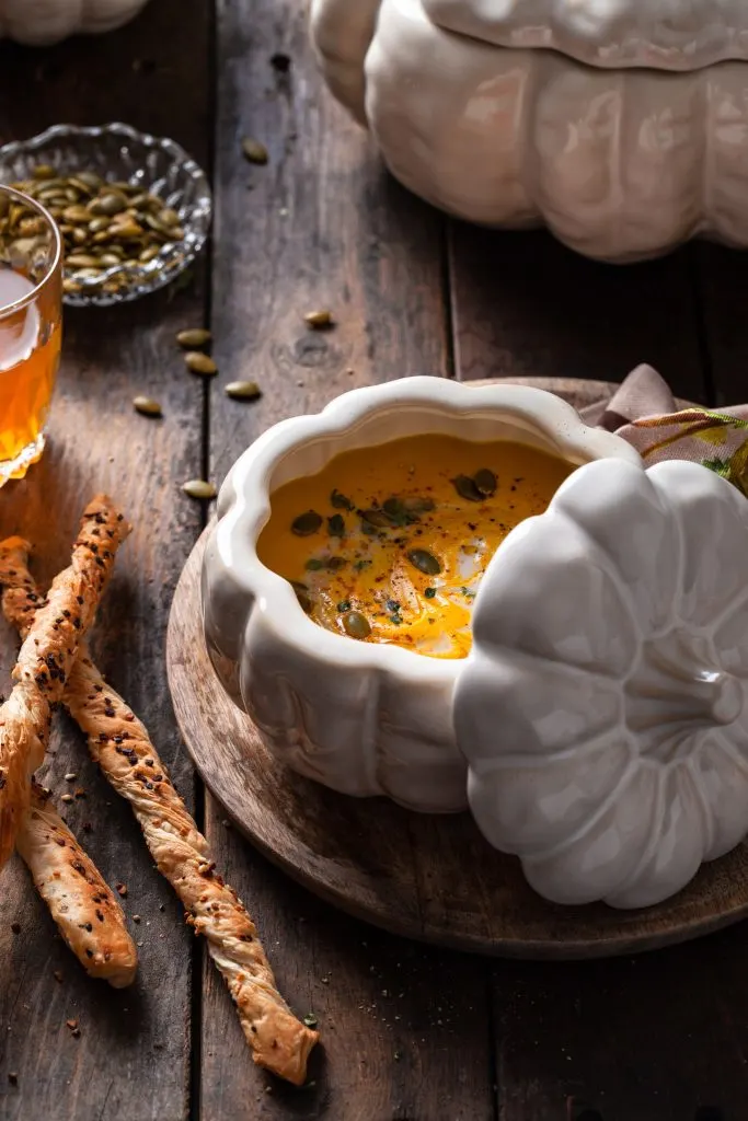 Pumpkin soup in a white pumpkin shaped bowl beside a pile of bread sticks.
