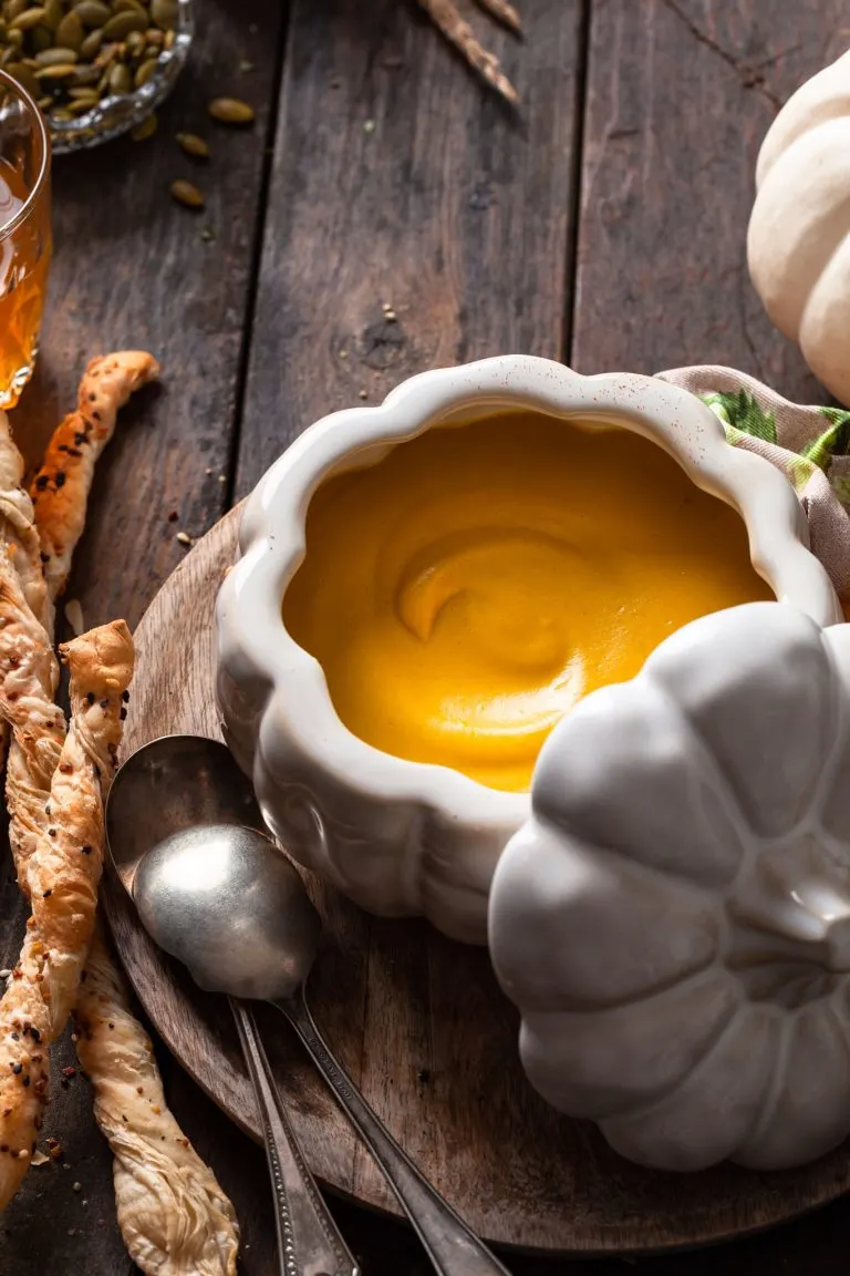 A white pumpkin shaped bowl filled with creamy roasted squash soup.