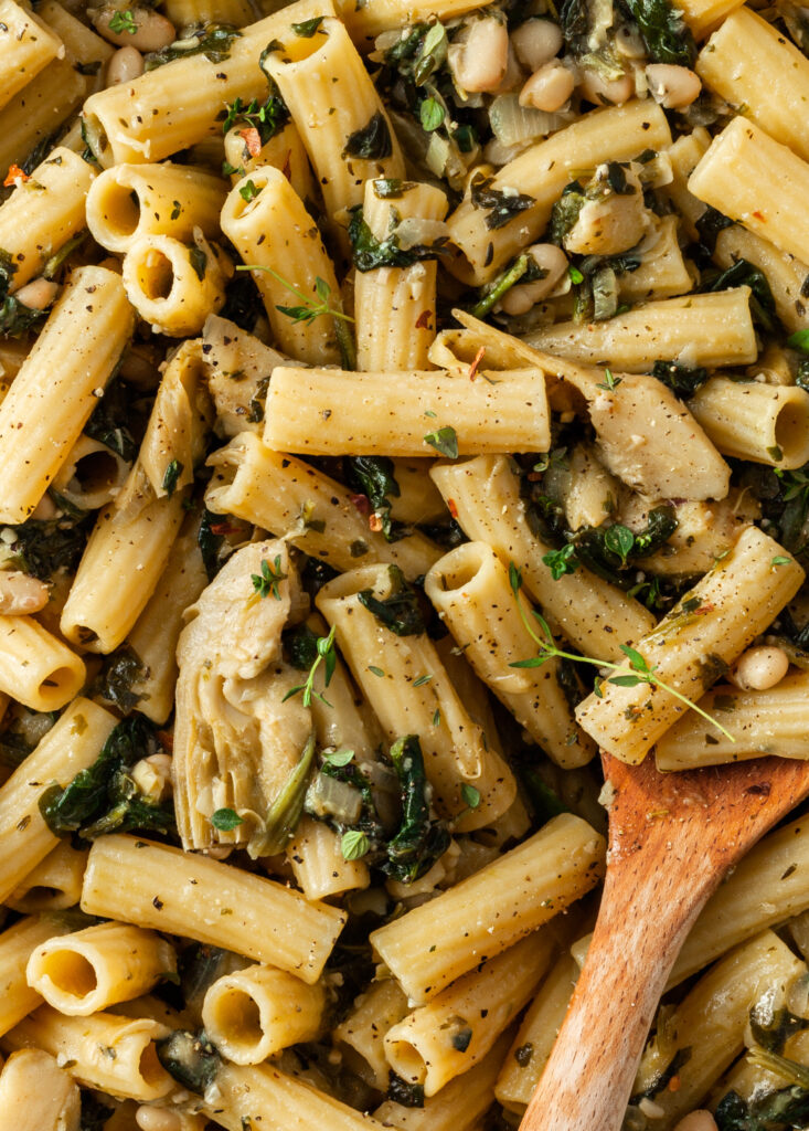 Close up of the spinach artichoke pasta in the pot being stirred with a wooden spoon. 